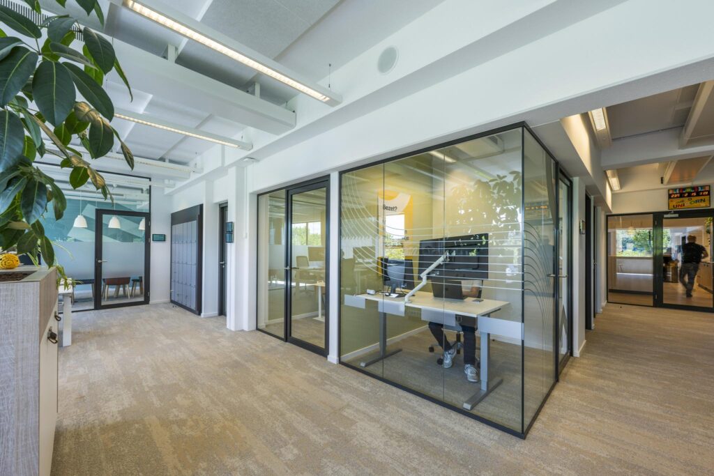 Modern office hallway with glass-walled meeting rooms and a person working at a desk on Mr. Treublaan.